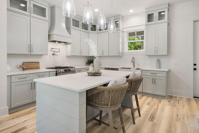 kitchen featuring a breakfast bar, custom exhaust hood, decorative backsplash, gas range, and a kitchen island
