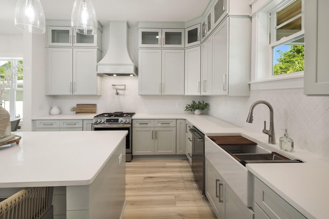 kitchen with light wood-style flooring, a wealth of natural light, custom exhaust hood, gas stove, and dishwashing machine
