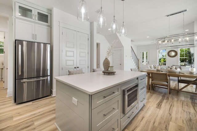 kitchen with light wood-style flooring, a center island, hanging light fixtures, open floor plan, and appliances with stainless steel finishes