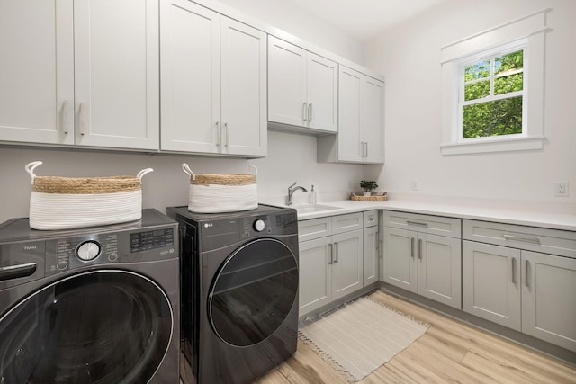 laundry room featuring washing machine and clothes dryer, light wood-style flooring, a sink, and cabinet space