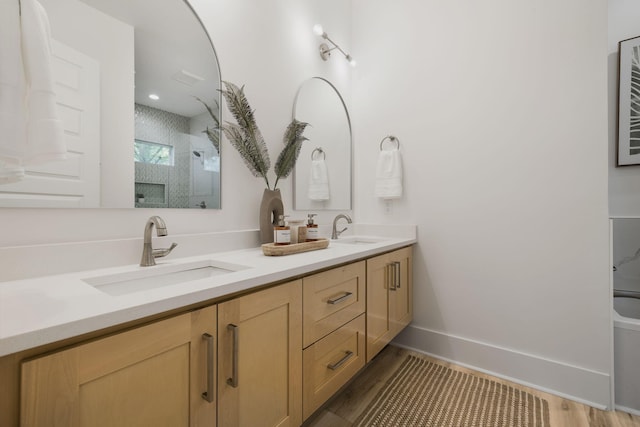full bath with a sink, a shower with shower door, double vanity, and wood finished floors