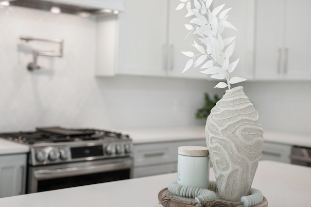 interior details with ventilation hood, stainless steel gas range oven, white cabinetry, and light countertops