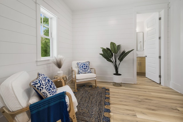 sitting room featuring baseboards, wood walls, and light wood-type flooring