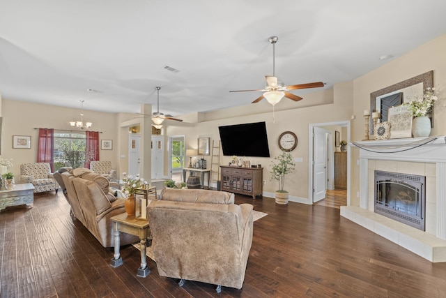 living room with visible vents, dark wood-type flooring, ceiling fan with notable chandelier, and a fireplace