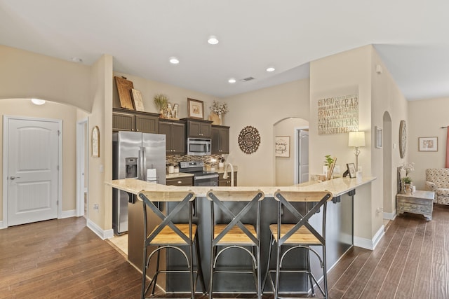kitchen featuring decorative backsplash, dark wood-style flooring, a kitchen breakfast bar, arched walkways, and appliances with stainless steel finishes