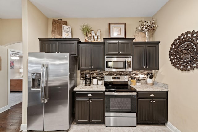 kitchen featuring baseboards, appliances with stainless steel finishes, decorative backsplash, and light stone counters