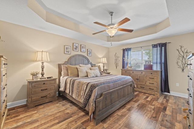 bedroom with wood-type flooring, a tray ceiling, and baseboards