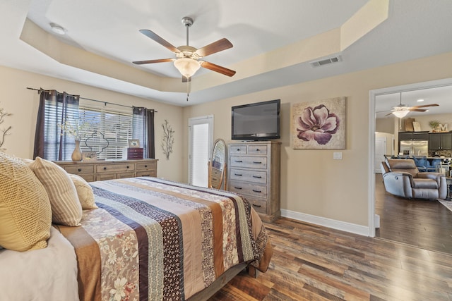 bedroom with visible vents, wood finished floors, baseboards, stainless steel fridge, and a tray ceiling