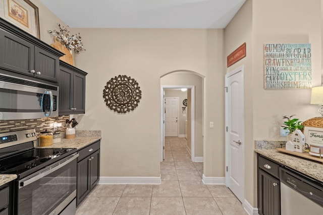 kitchen featuring arched walkways, backsplash, stainless steel appliances, and light stone counters