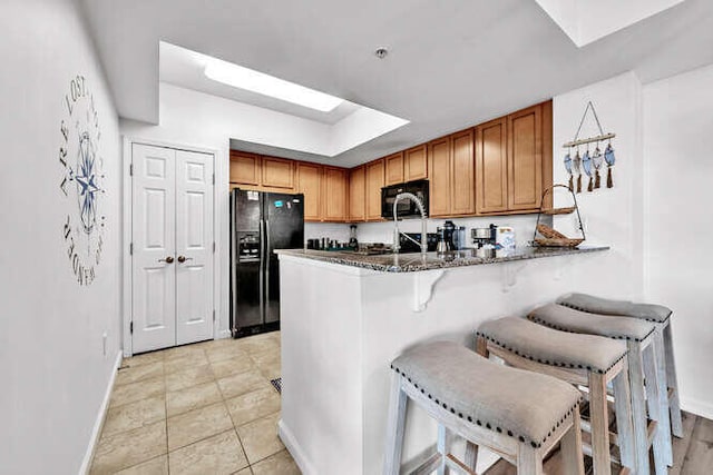kitchen with a peninsula, baseboards, a skylight, and black appliances