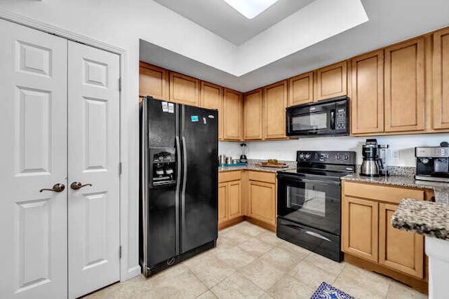 kitchen featuring stone countertops, brown cabinetry, and black appliances