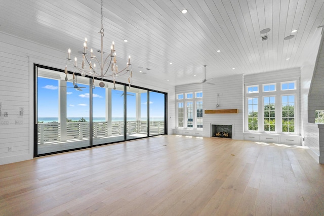 unfurnished living room featuring plenty of natural light, ceiling fan with notable chandelier, wood finished floors, and a fireplace