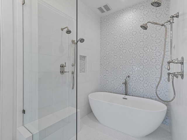 bathroom with visible vents, a freestanding bath, a tile shower, and tile walls