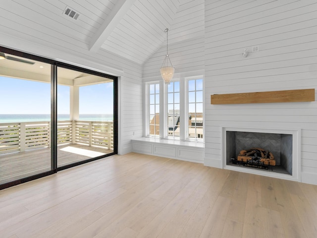 unfurnished living room featuring wooden walls, a large fireplace, light wood-style flooring, a water view, and visible vents