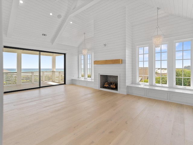 unfurnished living room featuring high vaulted ceiling, a chandelier, a wealth of natural light, and light wood-style flooring