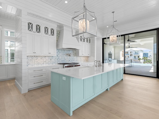 kitchen with decorative backsplash, light wood-style floors, light countertops, custom range hood, and ceiling fan with notable chandelier