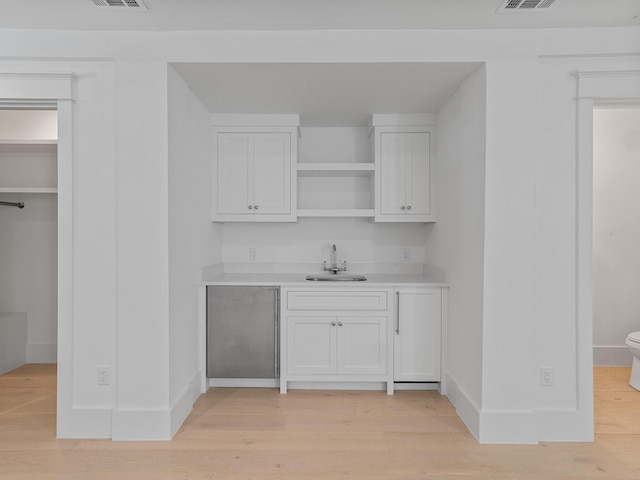 bar featuring visible vents, a sink, baseboards, indoor wet bar, and light wood-style floors