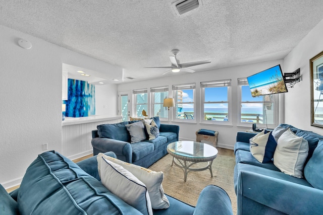 living room with a ceiling fan, a textured ceiling, baseboards, visible vents, and wood finished floors