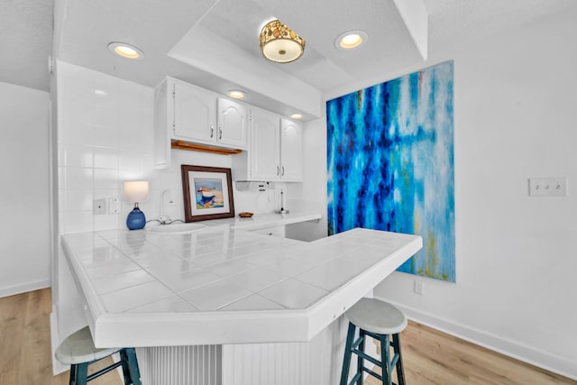 kitchen with baseboards, a breakfast bar, a sink, white cabinetry, and a peninsula