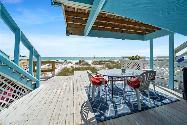 wooden terrace featuring a view of the beach, outdoor dining area, and a water view