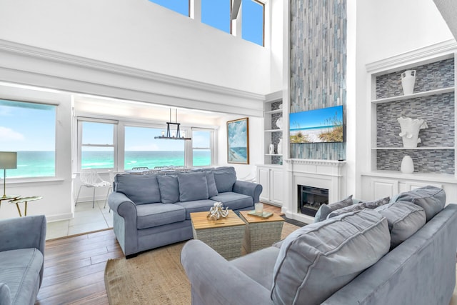 living area with baseboards, a glass covered fireplace, built in features, a towering ceiling, and hardwood / wood-style flooring