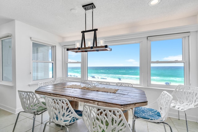 dining area featuring a notable chandelier, a textured ceiling, baseboards, light tile patterned flooring, and a water view