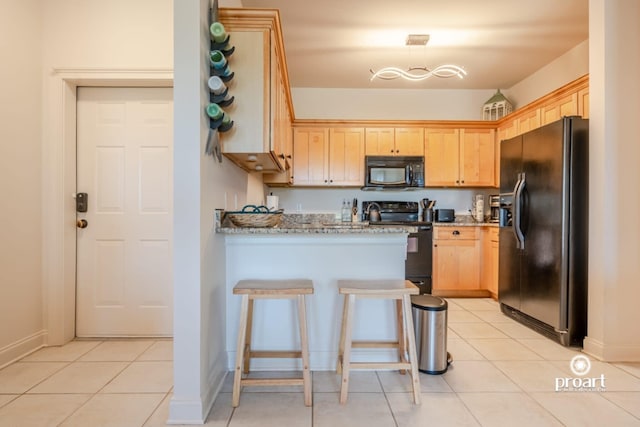 kitchen with light brown cabinetry, black appliances, a peninsula, and light stone counters