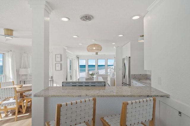 kitchen featuring freestanding refrigerator, white cabinetry, light stone countertops, and plenty of natural light