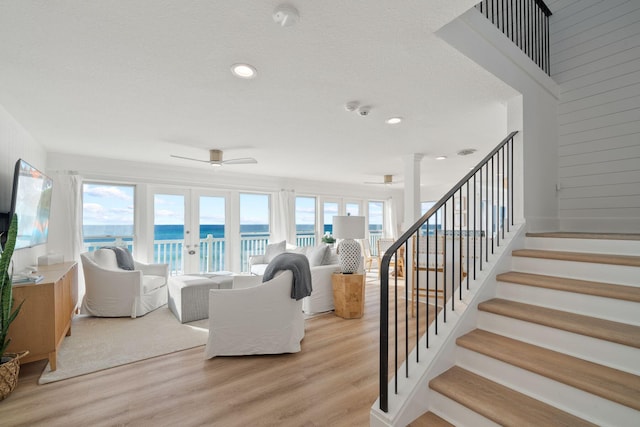 living area with light wood-style floors, a ceiling fan, stairs, and a water view