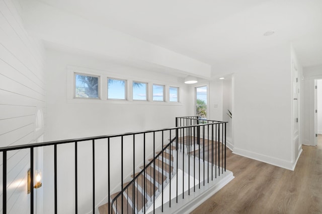 hall featuring baseboards, wood finished floors, and an upstairs landing