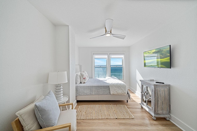 bedroom with baseboards, ceiling fan, a textured ceiling, and light wood-style flooring