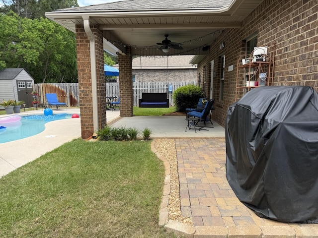 view of patio with ceiling fan, grilling area, a fenced backyard, a shed, and a fenced in pool