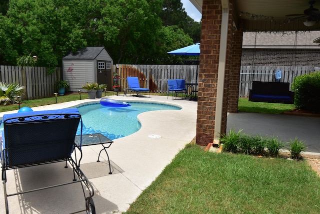 view of pool featuring a storage shed, a fenced backyard, a patio area, a ceiling fan, and an outdoor structure