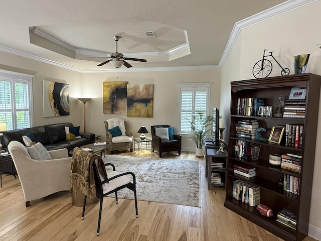sitting room featuring light wood-style floors, a ceiling fan, a tray ceiling, visible vents, and ornamental molding