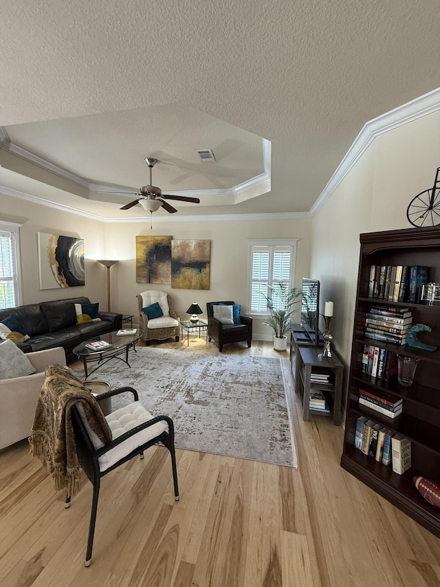 living area featuring crown molding, a textured ceiling, wood finished floors, and a tray ceiling