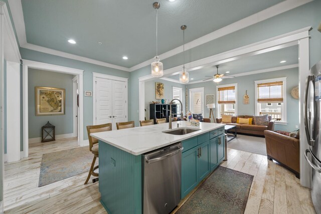kitchen featuring appliances with stainless steel finishes, a sink, green cabinetry, open floor plan, and an island with sink