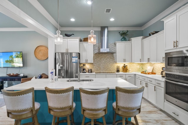 kitchen with stainless steel appliances, wall chimney range hood, backsplash, a sink, and white cabinetry