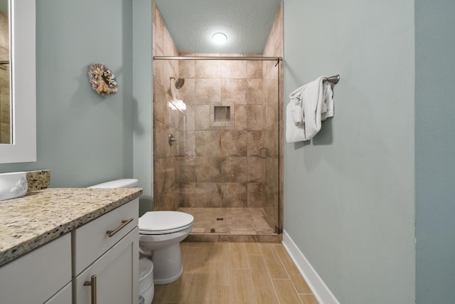 bathroom with a stall shower, vanity, toilet, and wood finished floors