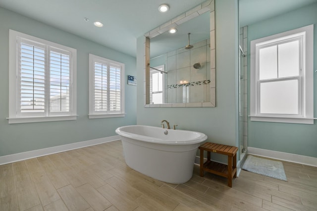 full bathroom featuring a stall shower, wood finished floors, baseboards, a freestanding bath, and recessed lighting