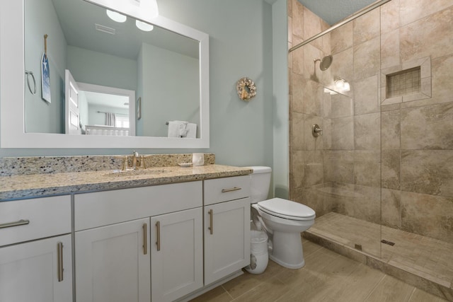 bathroom featuring toilet, tiled shower, and vanity