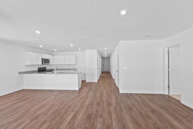 kitchen with a peninsula, open floor plan, white cabinets, a sink, and appliances with stainless steel finishes