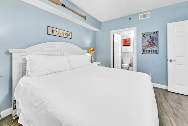 bedroom with baseboards, ensuite bathroom, visible vents, and wood finished floors