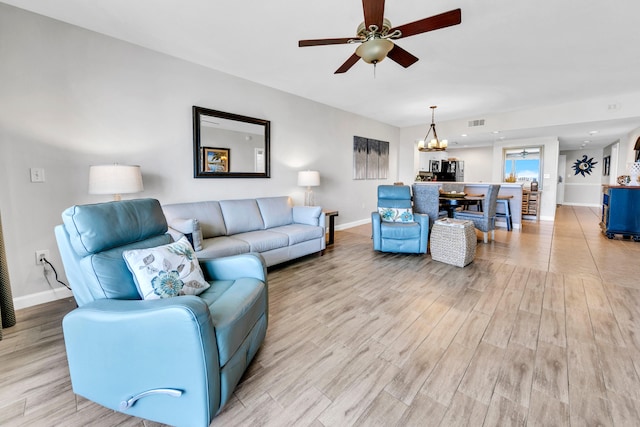 living room featuring baseboards, light wood-style flooring, visible vents, and ceiling fan with notable chandelier