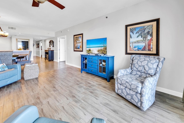 living area with baseboards, a ceiling fan, visible vents, and wood finished floors