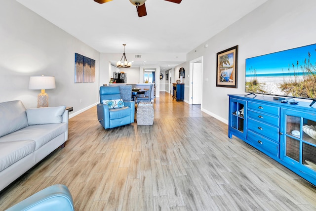 living area featuring ceiling fan with notable chandelier, baseboards, visible vents, and wood finished floors