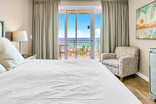bedroom with baseboards, a water view, wood finished floors, and access to exterior