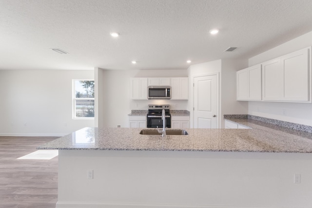 kitchen featuring white cabinets, light stone countertops, appliances with stainless steel finishes, light wood-style floors, and recessed lighting