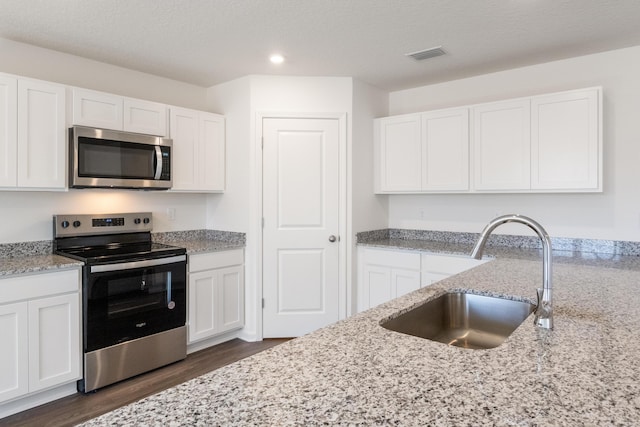kitchen featuring visible vents, a sink, white cabinets, dark wood-style floors, and stainless steel appliances