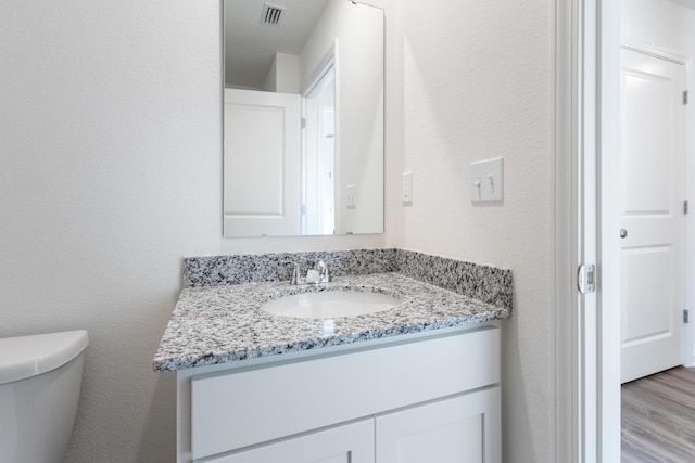 half bath featuring a textured wall, vanity, toilet, wood finished floors, and visible vents