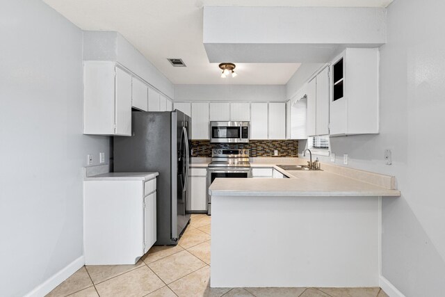 kitchen featuring a sink, light tile patterned floors, white cabinets, a peninsula, and stainless steel appliances